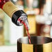 A bottle with a measured liquor pourer dispensing liquid into a metal container.
