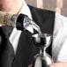 A close-up of a bottle with a measured liquor pourer dispensing liquid into a stainless steel jigger.
