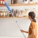 A woman using a Lavex telescoping wand with a duster sleeve to clean shelves.
