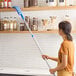 A woman using a Lavex Flex Wand Duster with a microfiber sleeve to dust shelves.