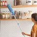 A woman in an orange shirt using a Lavex Flex Wand Duster with Chenille Sleeve on a grocery store shelf.