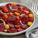 A plate of sliced beets garnished with cherry tomatoes, onions, and chives.