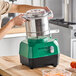 A green and black AvaMix Revolution Max combination food processor with a stainless steel bowl being placed on its base.