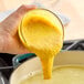 A hand pouring yellow Better Than Bouillon chicken flavor base into a pot of food.