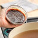 A hand using Better Than Bouillon Premium Roasted Beef Flavor Base to make brown liquid in a pot.