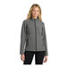 A woman wearing a Port Authority pearl gray heather soft shell jacket.