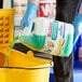 A person in blue gloves pouring Mr. Clean Professional degreasing floor cleaner into a yellow bucket.
