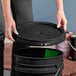 A hand opening a black plastic container with a round black lid.