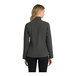 A woman wearing a black and charcoal heather Port Authority core soft shell jacket.
