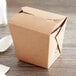 A brown Fold-Pak Earth take-out container with a lid on a wood surface.