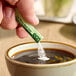 A hand holding a green and black ecoStick packet over a cup of coffee.