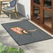 A rectangular gray entrance mat with a waffle texture and a 'Hot Coffee' design, placed outside a door.
