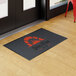 A rectangular black entrance mat with a customizable design, placed indoors near a door on a wooden floor.