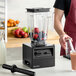 A person pouring fruit into a Blendtec commercial blender on a counter.
