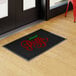 A rectangular black entrance mat with red and green lettering that reads 'Italian Pizza,' placed on a light wood floor near a glass door.