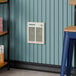 A Boltic steel electric fan-forced wall heater installed on a blue paneled wall.