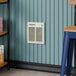 A Boltic steel electric fan-forced wall heater mounted on a blue paneled wall.