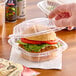 A hand holding a burger in a Dart clear hinged plastic container.