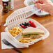 A hand holding a Dart clear hinged plastic take-out container with food inside.