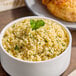 A white bowl filled with cooked whole grain millet garnished with herbs.