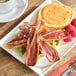 A plate with a Prime Roots Vegan Hickory Koji-Bacon sandwich and a cup of coffee on a table.