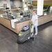 A person operating a Karcher BD 43/25 C BP 17-inch cordless walk-behind floor scrubber in a commercial kitchen or cafeteria setting.