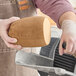 A man using a knife to cut Prime Roots Vegan Classic Smoked Koji-Turkey deli meat on a counter.