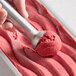 A hand using a metal scoop to serve Villa Dolce Rosanna Raspberry Sorbetto into a container.