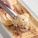 A hand scooping Villa Dolce Tiramisu Gelato into a metal pan on a counter.