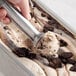 A person scooping Villa Dolce Traditional Cookies & Cream Gelato into a metal pan.