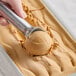 A hand using a metal scoop to scoop Villa Dolce Argentine Salted Dulce de Leche Gelato.