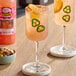 A pair of glasses of pink Master of Mixes Paloma drinks with jalapenos and orange slices on a table with a bowl of nuts.
