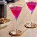Two martini glasses of lavender liquid on a table in a cocktail bar.