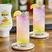 Two glasses of yellow and pink drinks on a table with a bottle of Real Yuzu Puree Infused Syrup.