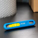 A Pacific Handy Cutter blue and yellow safety knife on a black surface.