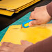 A person using a Pacific Handy Cutter Auto-Retract Volo blue safety knife to cut open a yellow envelope.
