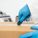 A person in blue gloves using a Pacific Handy Cutter Auto-Retract Volo Safety Knife to cut a box.