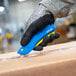 A person in gloves using a Pacific Handy Cutter blue and yellow safety knife.