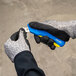 A gloved hand holds a blue Pacific Handy Cutter Auto-Retract Rebel safety knife.