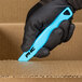A person in black gloves using a Pacific Handy Cutter blue safety knife to cut a cardboard box.