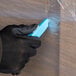 A person wearing black gloves using a Pacific Handy Cutter Dart Hi-Viz Blue safety cutter to cut plastic wrap.