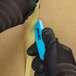 A person in black gloves using a Pacific Handy Cutter blue safety cutter.