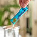 A hand holding a blue Sqwincher QwikStik Zero Mixed Berry drink mix over a glass.