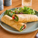 Two Celia's Vegan Jalapeno Cheddar flour tortillas on a plate with a salad and a glass of water.