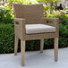 An Outdoor Interiors wicker dining armchair with a beige cushion on it.