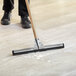 A person using a Lavex black neoprene foam floor squeegee with metal frame and adapters to clean the floor.