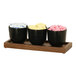 A Cal-Mil walnut condiment organizer with three black cups holding packets on a wooden tray.