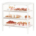A white metal Cal-Mil bakery display case filled with pastries and cupcakes displayed behind glass.