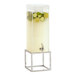 A Cal-Mil beverage dispenser with cucumber and lime slices in the ice chamber on a chrome metal base.