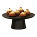 A black Cal-Mil cake pedestal displaying food on a table.